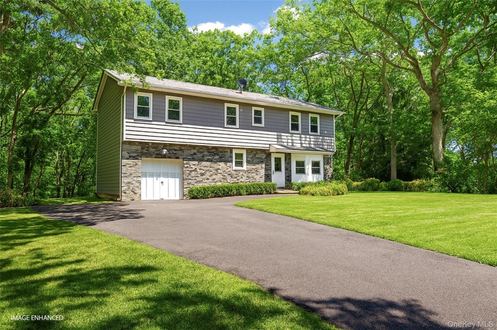 Colonial inspired home with a garage, asphalt driveway, a front lawn, and stone siding
