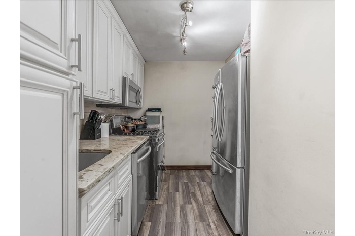 Kitchen with white cabinets, appliances with stainless steel finishes, light stone counters, and backsplash