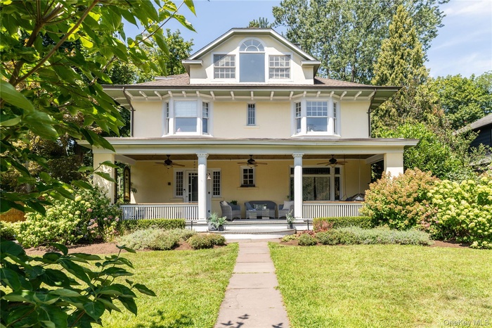 American foursquare style home with a ceiling fan, stucco siding, covered porch, a front lawn.