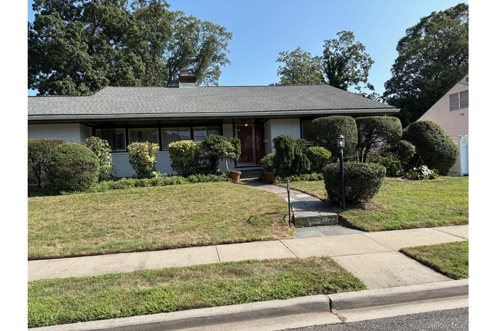 Single story home with a front yard, brick siding, a shingled roof, and a chimney