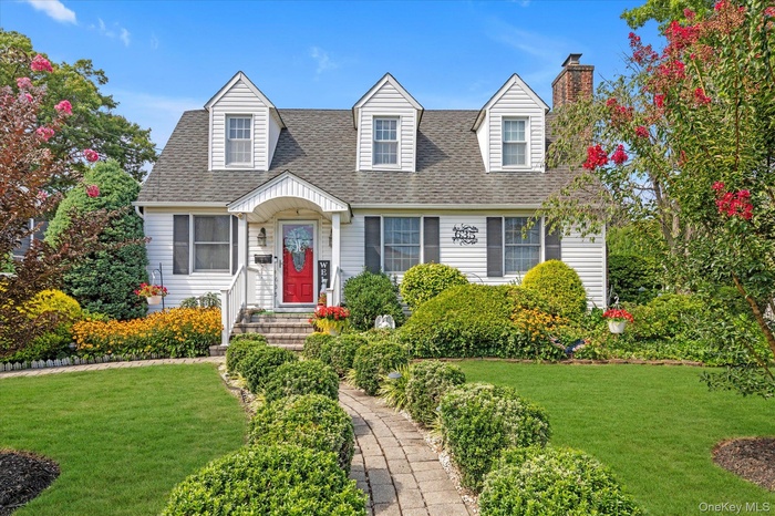 Cape cod-style house featuring a shingled roof and a front yard