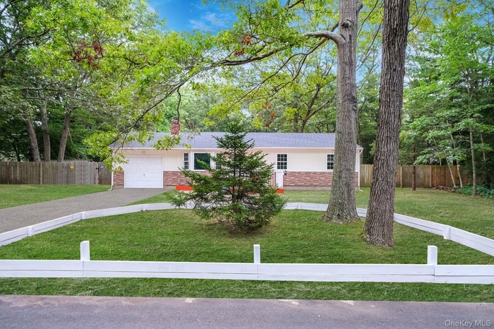 Single story home featuring brick siding, an attached garage, a chimney, driveway, and view of scattered trees