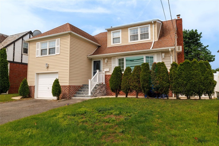 View of front of house with a chimney, a front lawn, a garage, driveway, and a shingled roof