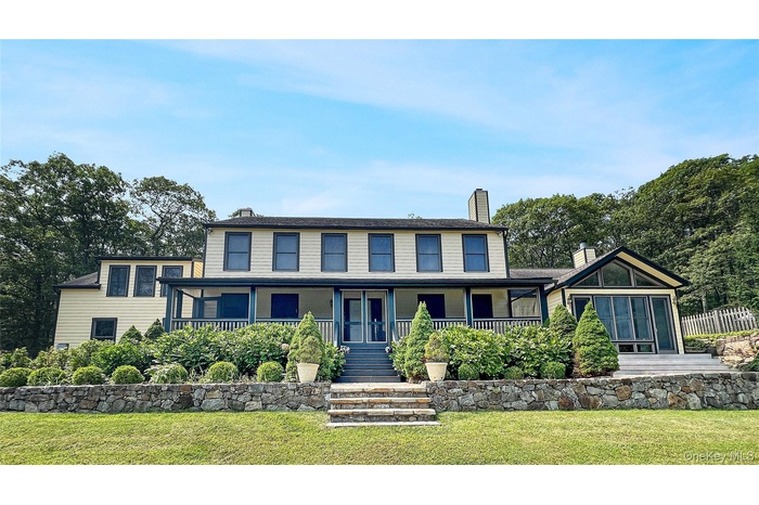 View of front of home with covered porch, a chimney, a front lawn, and stairs