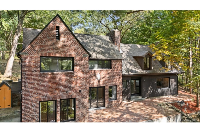 Front view of house featuring a chimney, brick siding, a shingled roof, and a patio area