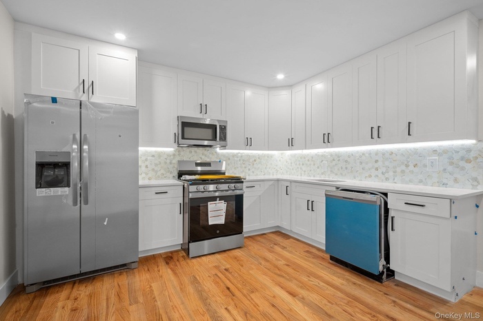 Kitchen featuring appliances with stainless steel finishes, white cabinetry, light wood finished floors, backsplash, and recessed lighting