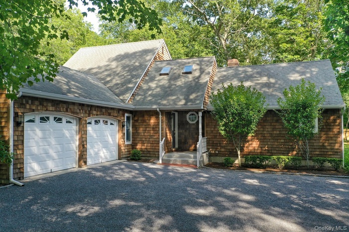 Shingle-style home featuring an attached garage, driveway, roof with shingles, and a chimney