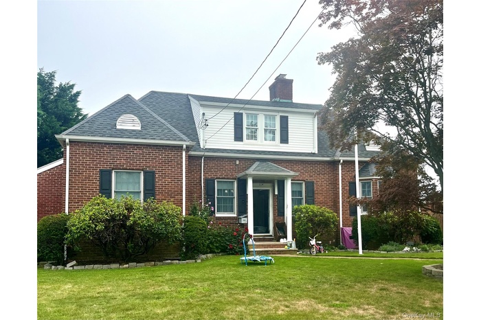 Traditional home featuring a front yard, brick siding, a chimney, and a shingled roof