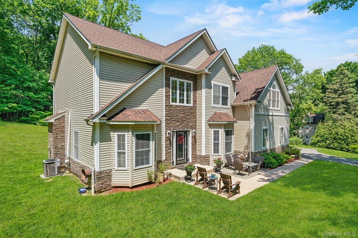 Traditional-style house with stone siding, a front lawn, roof with shingles, and a patio area