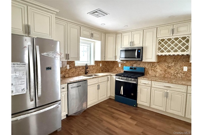 Kitchen featuring appliances with stainless steel finishes, dark wood finished floors, tasteful backsplash, and light stone counters