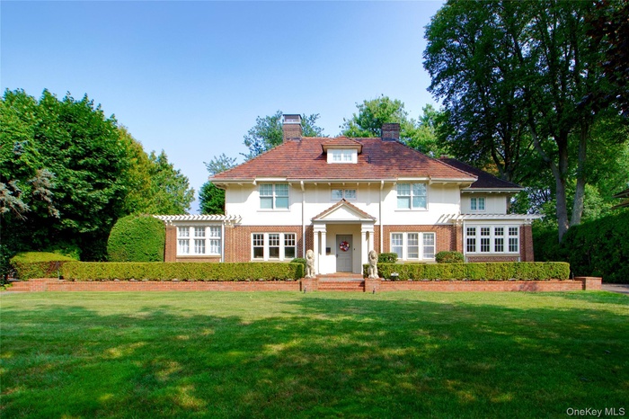 View of front of home with a chimney, brick siding, and a front lawn