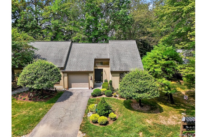 Mid-century modern home with roof with shingles, driveway, board and batten siding, an attached garage, and a front lawn