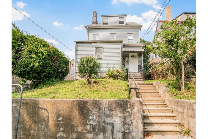 View of front of house with a front yard, a chimney, and stairway