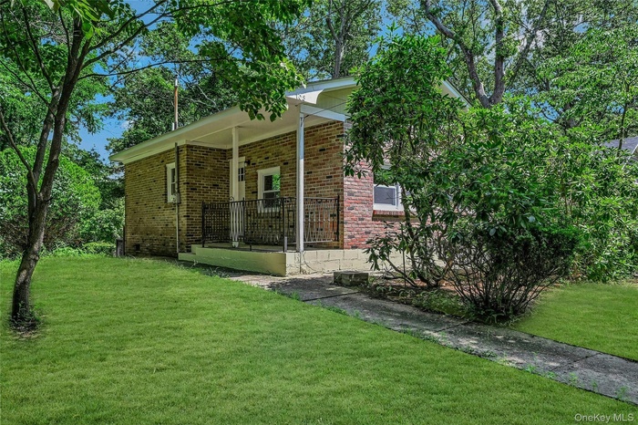 View of front of property with brick siding, a front yard, and covered porch