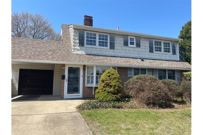 View of front of property with brick siding, a chimney, concrete driveway, an attached garage, and roof with shingles