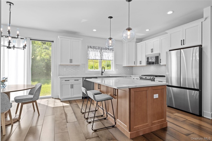 Kitchen featuring stainless steel appliances, backsplash, a center island, wood finished floors, and white cabinetry