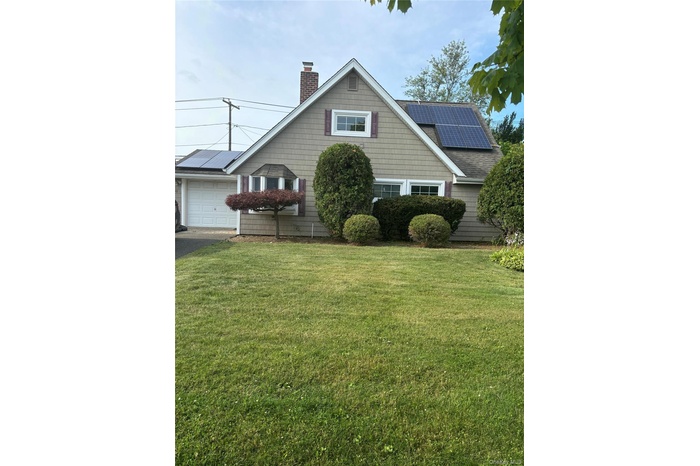 View of front of house featuring solar panels, a chimney, a front yard, and an attached garage