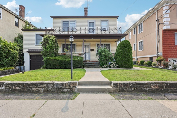 View of front of home with a balcony, a front yard, a chimney, and covered porch
