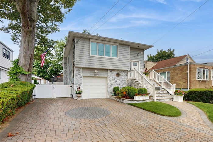 View of front facade with a gate, stone siding, an attached garage, and decorative driveway