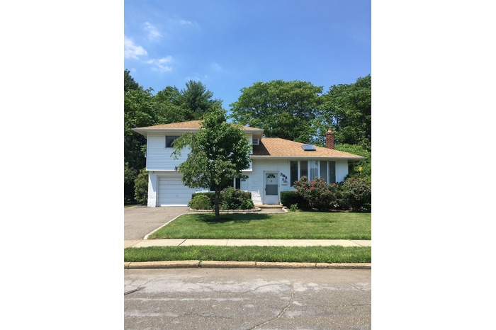 View of front of property with a front yard, asphalt driveway, a chimney, and an attached garage