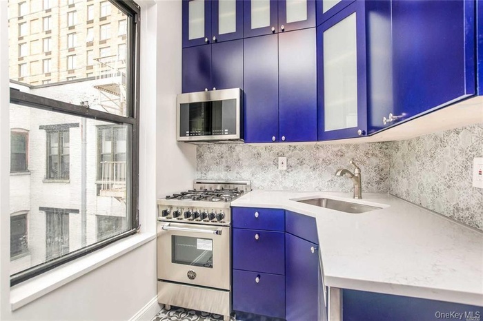 Kitchen featuring appliances with stainless steel finishes, backsplash, light countertops, glass insert cabinets, and blue cabinetry