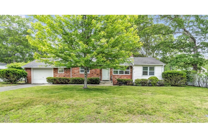 View of property hidden behind natural elements featuring driveway, an attached garage, brick siding, and a chimney