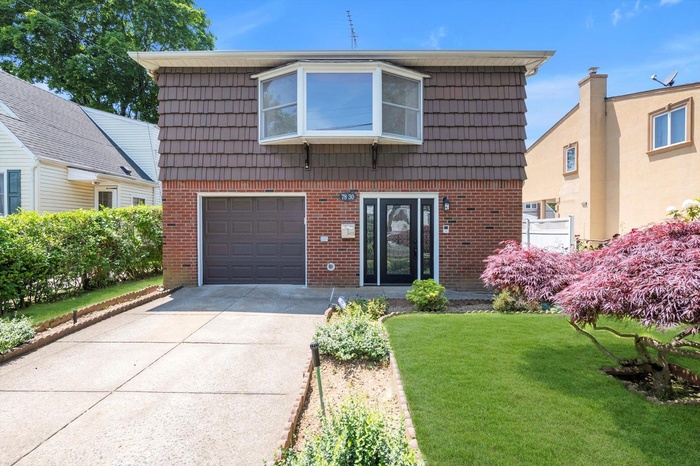 View of front facade with brick siding, a garage, driveway, mansard roof, and a front lawn