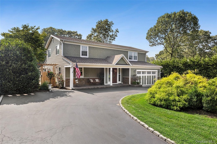 View of front of home with driveway, stone siding, a shingled roof, a porch, and a front yard