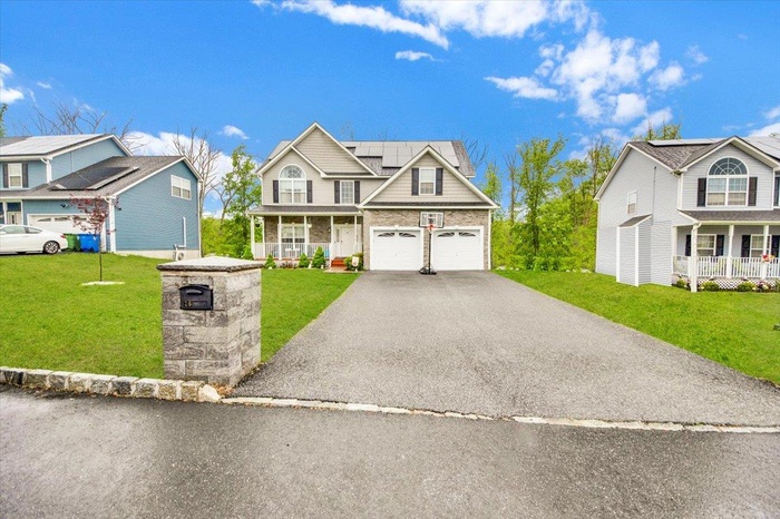 Traditional-style home with covered porch, roof mounted solar panels, asphalt driveway, a front lawn, and brick siding