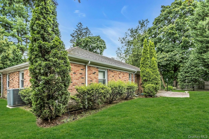 View of side of home with a yard, brick siding, a shingled roof, and a patio