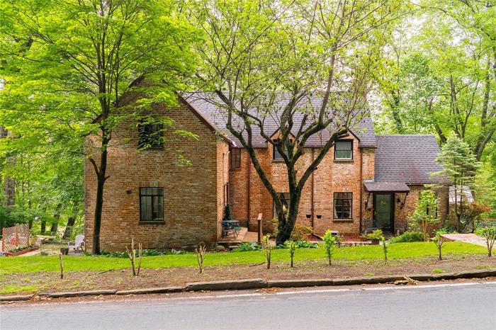 Tudor home featuring roof with shingles, brick siding, and a front lawn