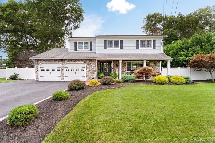 View of front of property with stone siding, driveway, a chimney, covered porch, and a shingled roof