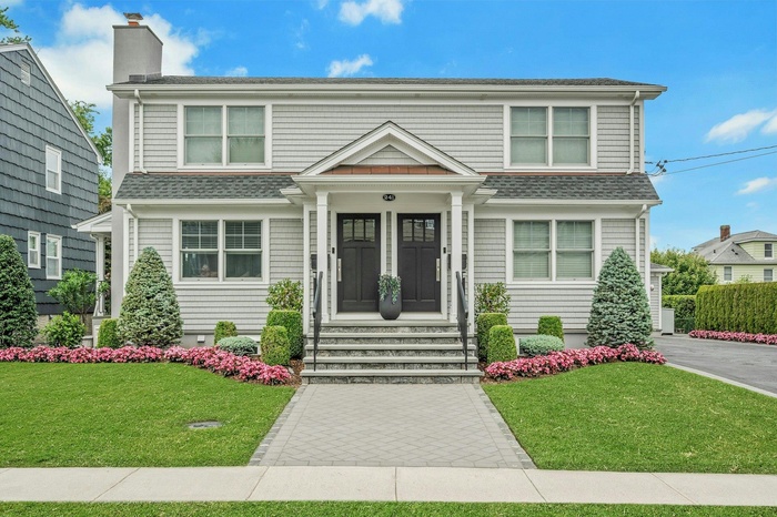 View of front facade featuring a front lawn, a shingled roof, and a chimney