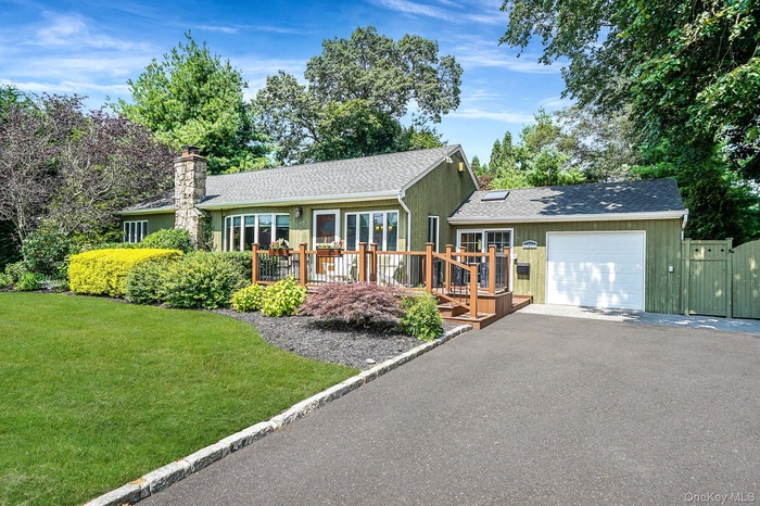 Single story home with a garage, a deck, roof with shingles, driveway, and a front lawn