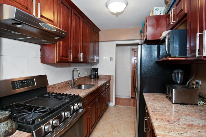 Kitchen with gas stove, extractor fan, a sink, light stone counters, and dark brown cabinets