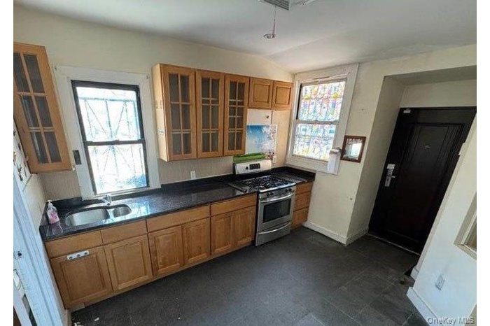 Kitchen featuring brown cabinets, stainless steel gas range, dark stone countertops, vaulted ceiling, and glass insert cabinets