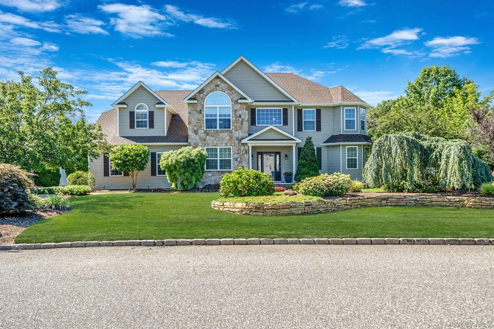 Colonial inspired home featuring stone siding, a front yard, and roof with shingles