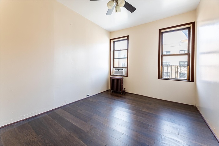 Spare room featuring cooling unit, dark wood-type flooring, ceiling fan, and radiator