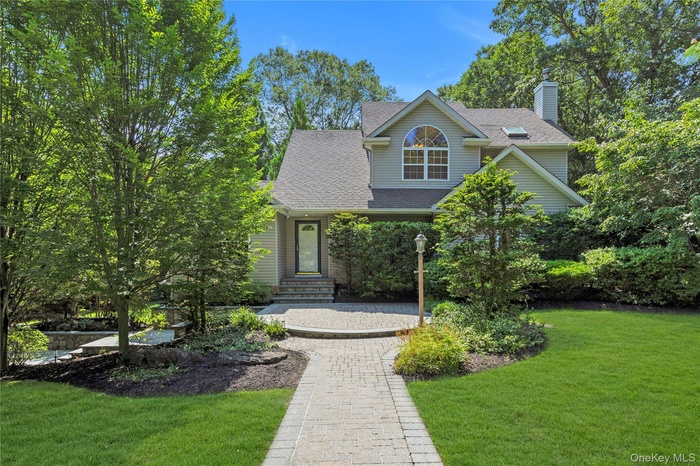 View of front facade featuring a front yard, a shingled roof, and a chimney