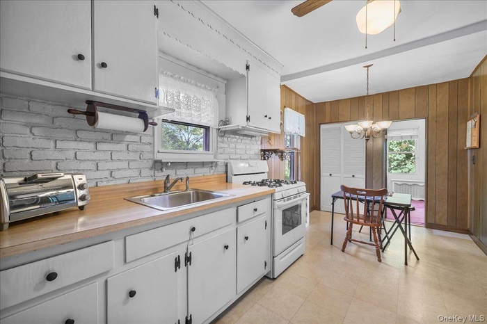 Kitchen with white range with gas stovetop, a sink, light countertops, wooden walls, and healthy amount of natural light