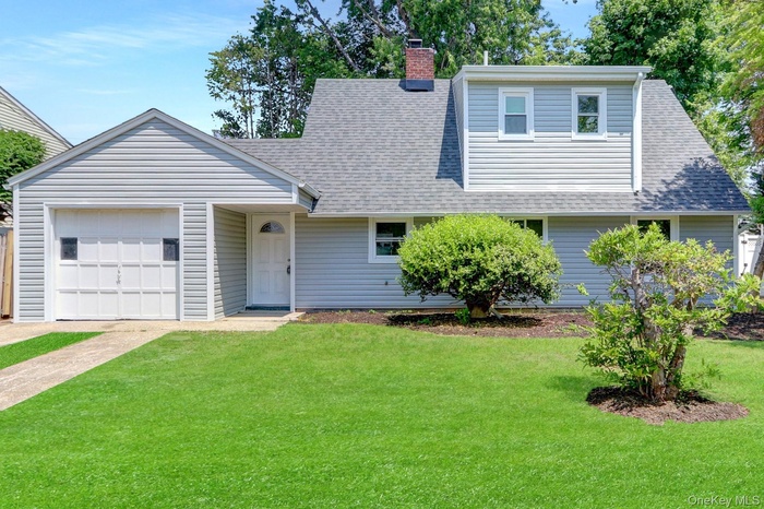 View of front of property with a garage, a front lawn, roof with shingles, a chimney, and driveway