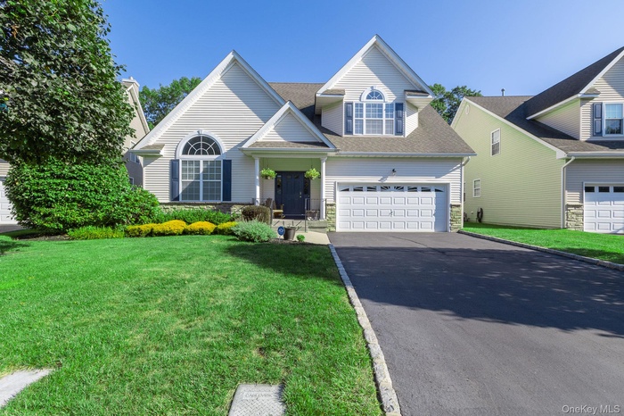 Traditional-style home featuring stone siding, driveway, roof with shingles, a front lawn, and a garage