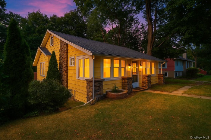 Bungalow-style home featuring stone siding, a front yard, and roof with shingles
