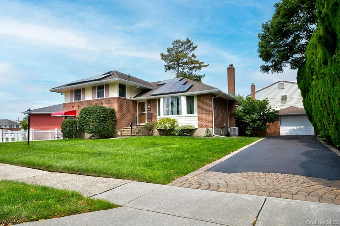 Split level home with brick siding, a front yard, and solar panels