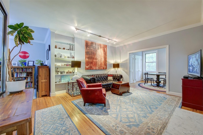 Living area featuring rail lighting, ornamental molding, light wood-style flooring, and built in features