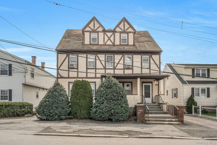 English Tudor-style home with stucco siding, shingled roof and covered porch.