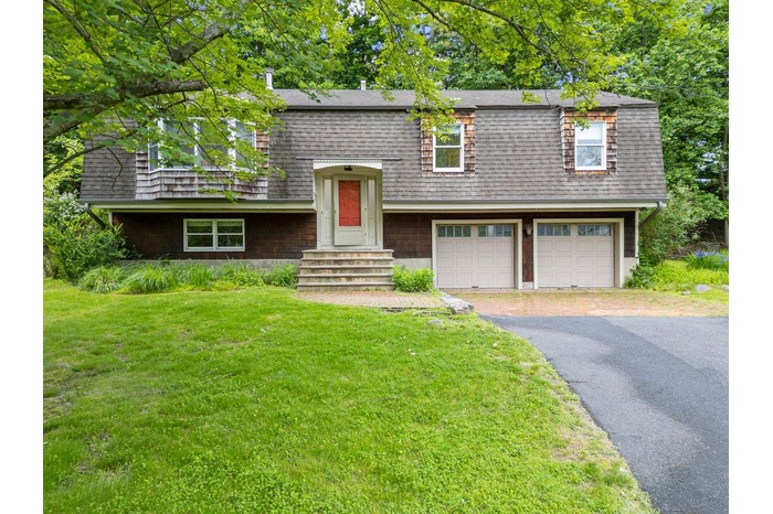 View of front facade featuring an attached garage, a front lawn, asphalt driveway, and roof with shingles