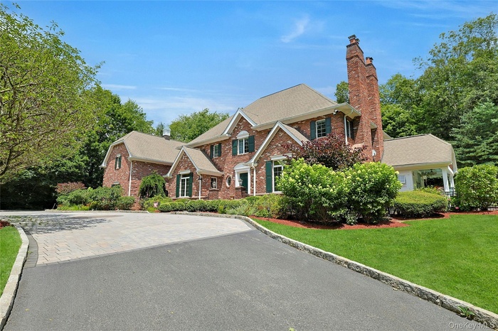 View of front of property with a chimney, a front yard, brick siding, and roof with shingles