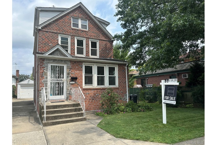 Traditional-style house with a front yard, brick siding, an outdoor structure, and a detached garage