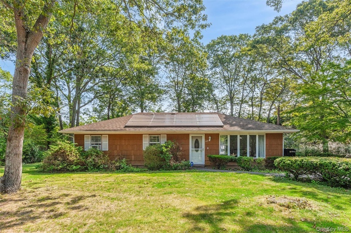 View of front of home with a front lawn, roof mounted solar panels, and roof with shingles